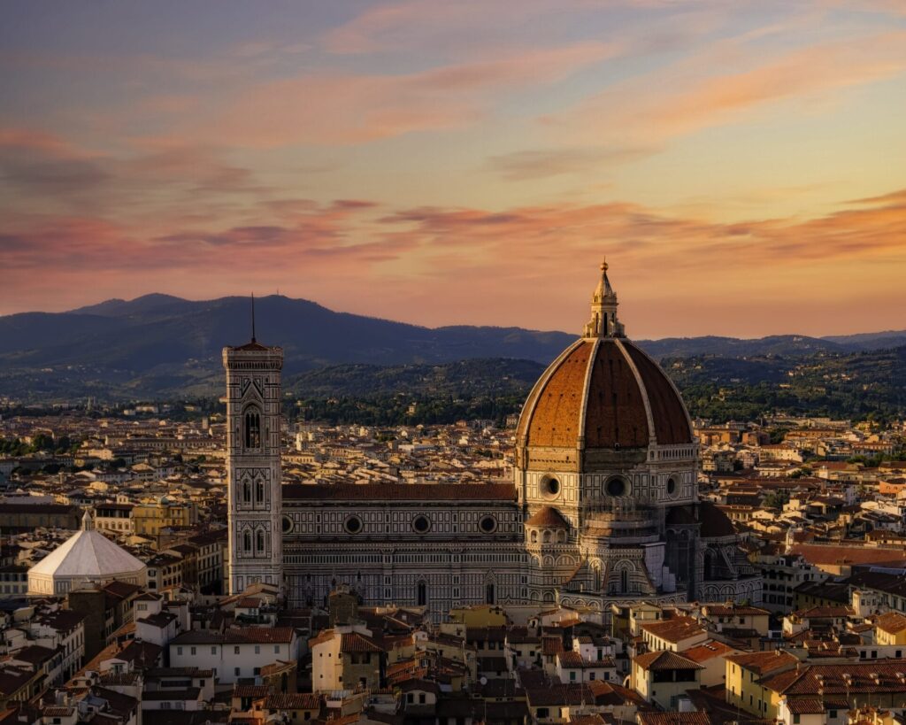Vista aerea del Duomo di Firenze con la sua iconica cupola e il campanile, sullo sfondo delle colline e del cielo al tramonto, che cattura la bellezza senza tempo che ispira la visione creativa di SHM Studio.